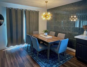 A dining area with a wooden table, blue chairs, a potted plant, and a modern pendant light. - Remodeled 4BR near Maidu Park · Roseville/Granite Bay · Pets OK (Roseville)