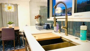 Een moderne keuken met een roestvrijstalen spoelbak, een houten aanrecht en een eethoek met een stoel en een tafel.