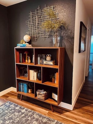 A modern living room with a dark wall, a wooden bookshelf, and a patterned rug.
