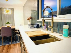 A modern kitchen with a stainless steel sink, a wooden countertop, and a window with a view of trees.