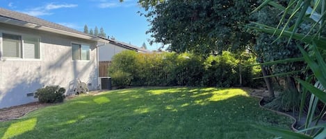 Una propiedad residencial con un césped bien cuidado, una casa de fachada blanca y un árbol grande que proporciona sombra.