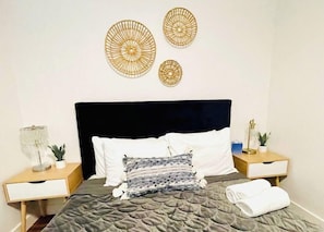 A neatly made bed with a dark headboard, two bedside tables with lamps, and decorative wall art.