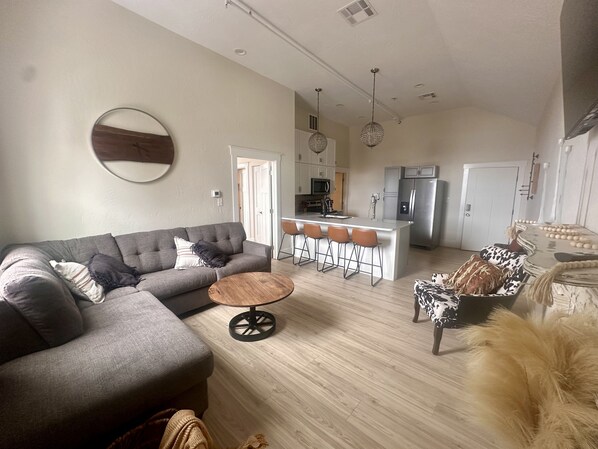 A modern living room with a grey sofa, a round coffee table, and a patterned ottoman. - Opera House Suite 1 (Kemmerer)