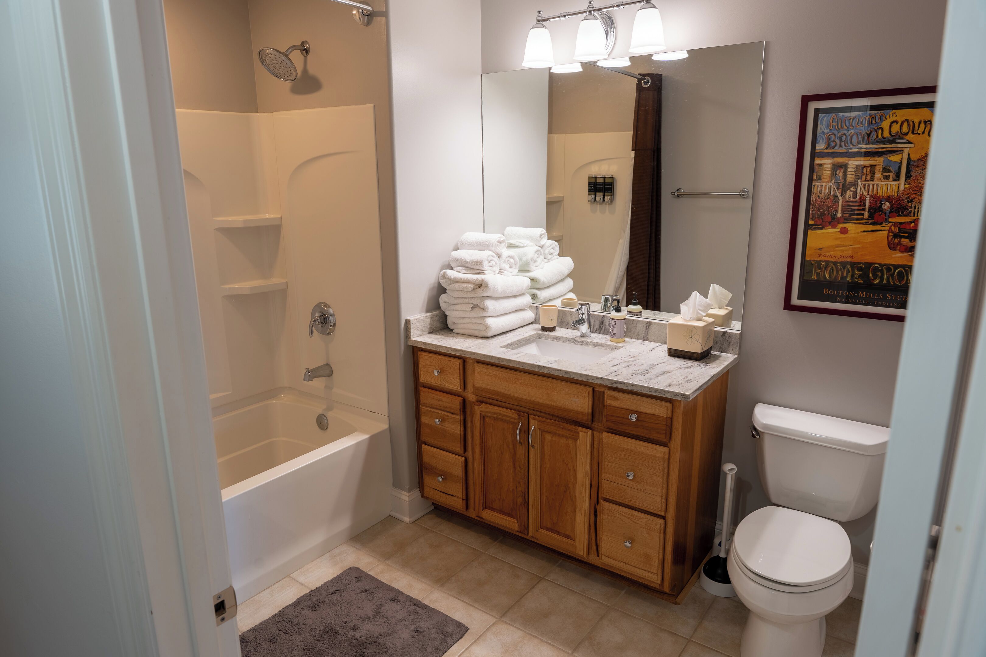 A modern bathroom with a bathtub, a sink with a marble countertop, wooden cabinets, and a toilet.