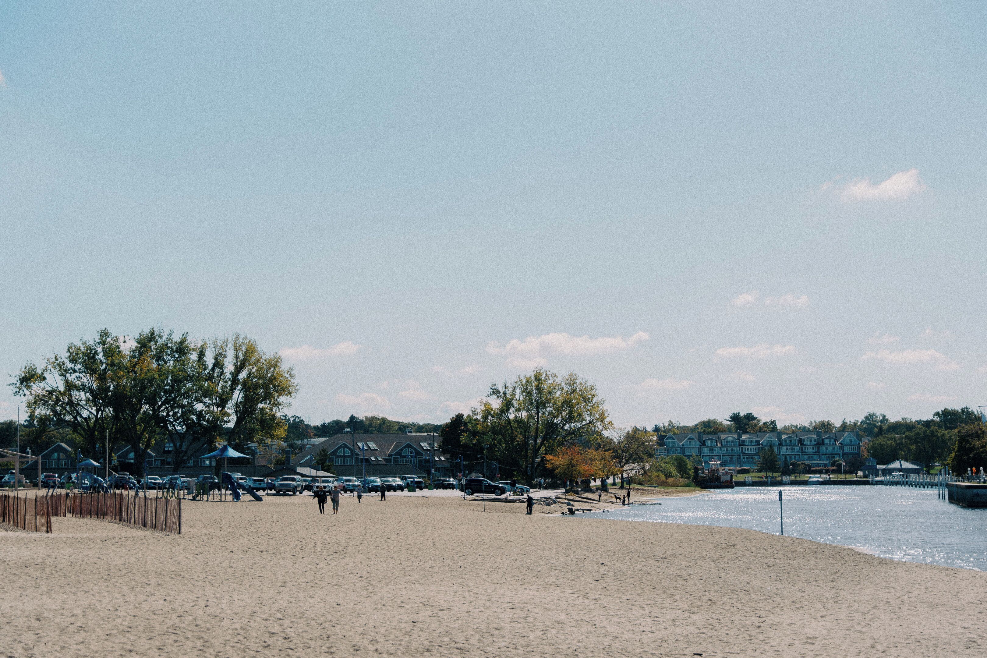 Een strand met een zandstrand, enkele mensen en een rij huizen op de achtergrond.
