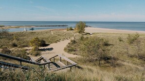Ein Strand mit einer Holzpromenade, die zu einem Sandbereich führt, einem Leuchtturm in der Ferne und ruhiger See.
