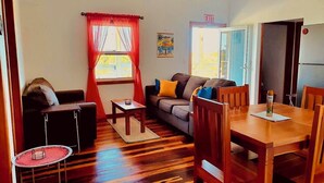 A cozy living room with a sofa, a small table, and a dining area with chairs. - Enjoy Secret Beach sunsets, fully equipped 3bd house, large deck, AC, WiFi,  (San Pedro)