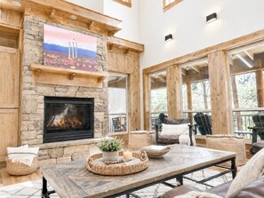 A spacious living room with a stone fireplace, comfortable seating, and large windows.