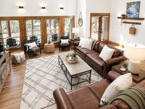 A spacious living room with leather sofas, a coffee table, and a large window providing natural light.