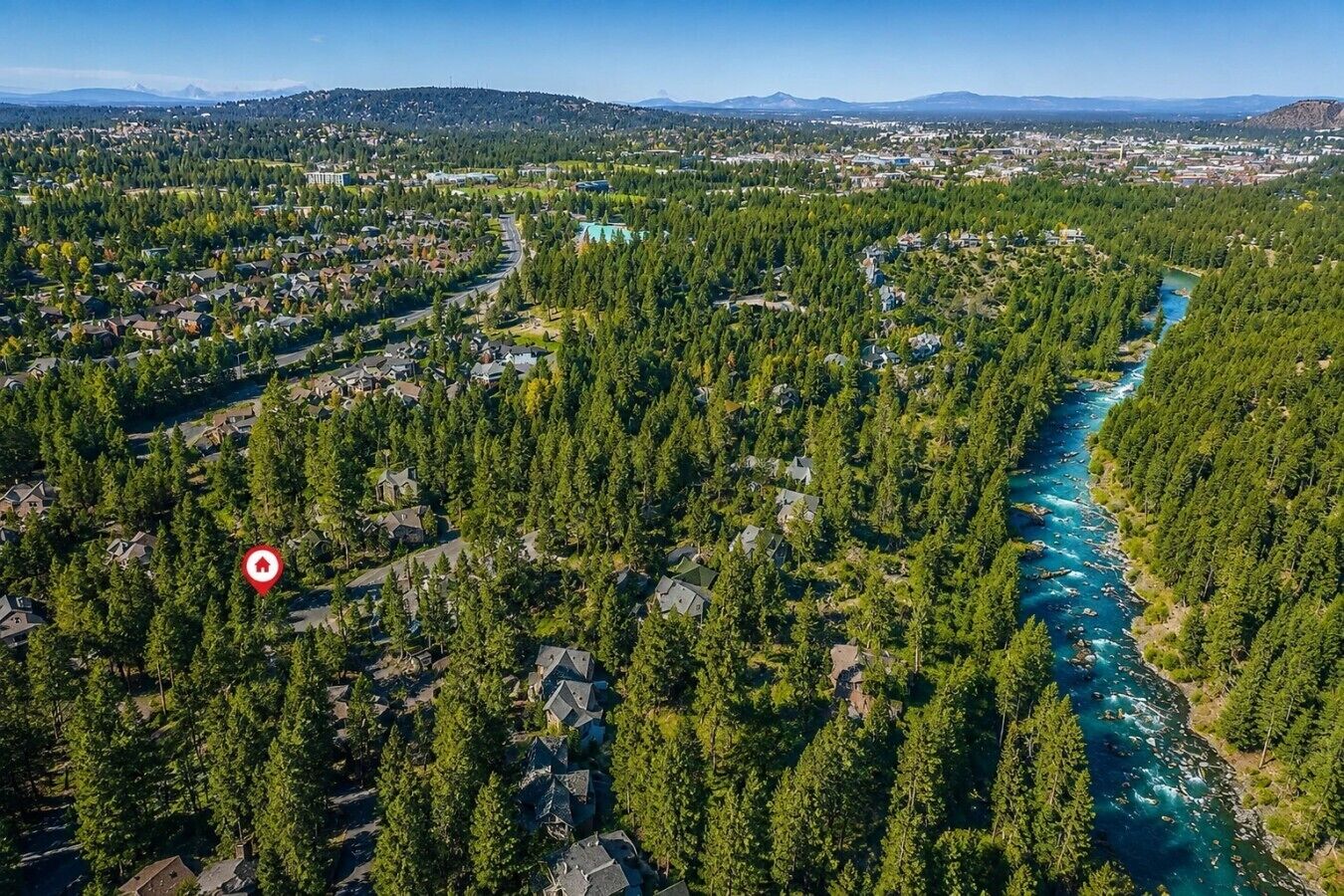 An aerial view of a residential area with a river running through it, surrounded by dense forests.