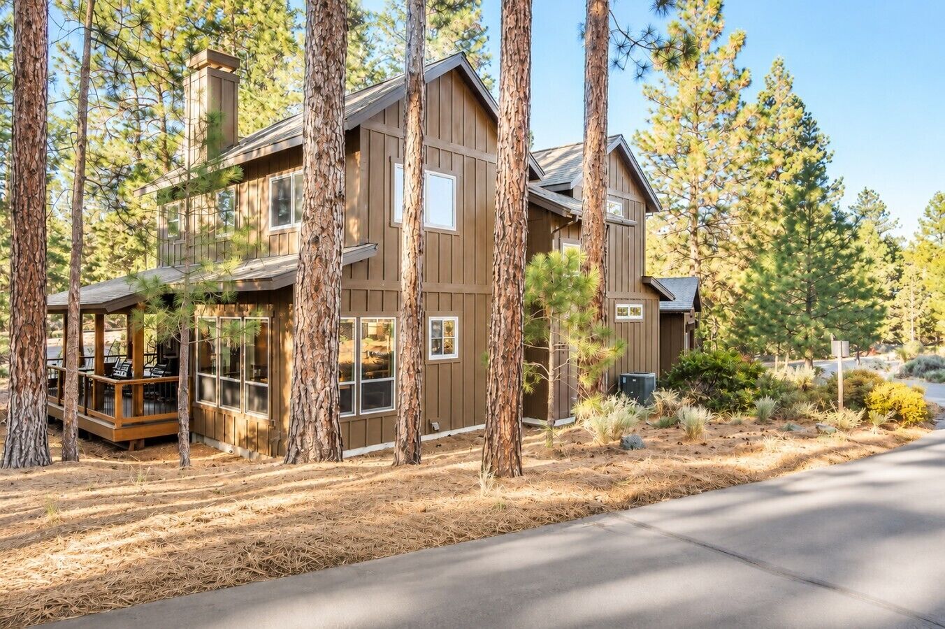 A two-story wooden cabin with a deck and large windows, surrounded by pine trees.