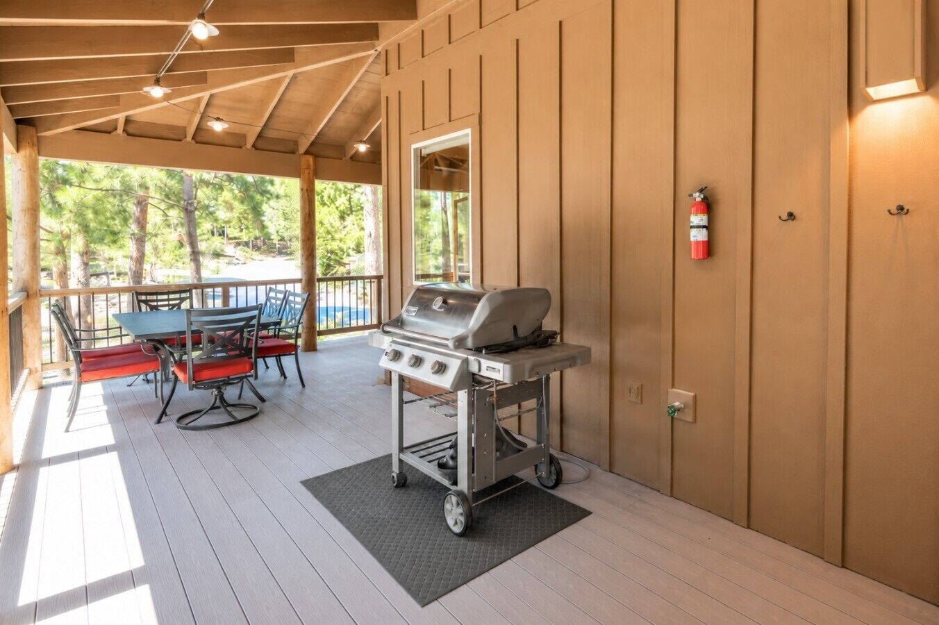 An outdoor covered patio with a barbecue grill, seating area, and a fire extinguisher on the wall.