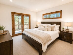 A bedroom with a large bed, wooden headboard, two bedside tables, a nightstand, and a window with a view of trees. - Serenity Retreat: Near Mt. Bachelor with Pool, Spa, River & Outdoor Trails (Bend)