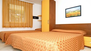 Hotellihuone, jossa on kaksi sänkyä, puinen pääty, keltainen kaappi ja ikkuna, jossa on läpikuultavat verhot.