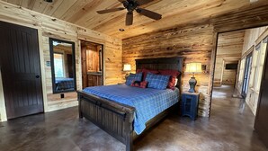 Dormitorio de una cabaña de madera con cama, ventilador de techo y mesita de noche.