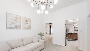 A modern living room with a sofa, two floral paintings, and a ceiling light fixture. - Contemporary Haven Retreat w/ KING BED Suite (Amarillo)