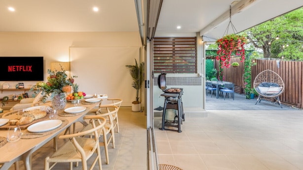 Una cocina moderna con horno empotrado, una zona de comedor con una mesa larga y sillas, y un televisor montado en la pared.