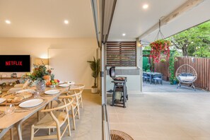 A modern kitchen with a built-in oven, a dining area with a long table and chairs, and a TV mounted on the wall. - Private Luxury Haven: SUV Hire, Pool, Near Marina (Trinity Park)