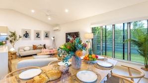 Comedor con mesa dispuesta para cuatro personas, sillas alrededor y un amplio ventanal con vista a la vegetación.