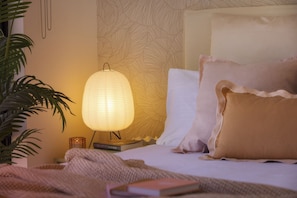 Un llit ben fet amb un capçal estampat, una làmpada de nit i un llibre damunt una taula de nit.