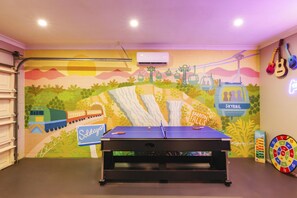 Una habitació amb una taula de ping-pong, un mural d'un tren i una cascada, i un aire condicionat fixat a la paret.