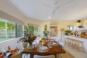 Comedor con una mesa de madera dispuesta para una comida, rodeada de sillas blancas, y un ventilador de techo.