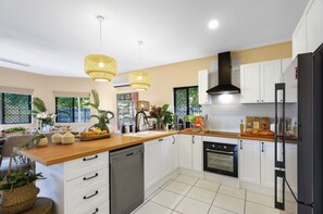 Une cuisine moderne avec des meubles blancs, un plan de travail en bois, un lave-vaisselle, un four et des luminaires suspendus.