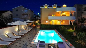 A pool area with lounge chairs and umbrellas, a large pool, and a multi-story building with balconies. - Amazing apartment in Zadar (Zadar)