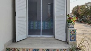 A room with a sliding door leading to a bed with a patterned bedspread. There is a small table with a potted plant beside the door. - Room with chromotherapy shower separate entrance (Alcamo)