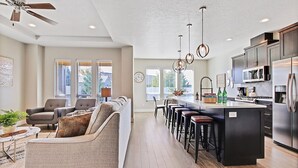 A modern kitchen with a central island, bar stools, and a seating area with a sofa and chairs. - 2 Adjacent Modern Homes - Sleep 16-20 - Near Shops, Dining, Parks, Entertainment (Meridian)