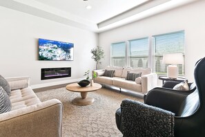A modern living room with a sofa, armchairs, a coffee table, and a TV mounted on the wall.