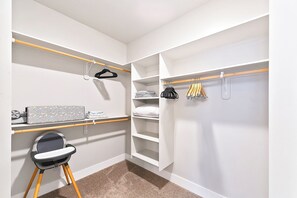 Un vestidor amplio con repisas abiertas, un sillón y ropa colgada.
