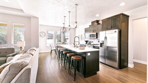A modern kitchen with a central island, bar stools, a stainless steel refrigerator, and pendant lighting. - 2 Adjacent Modern Homes - Sleep 16-20 - Near Shops, Dining, Parks, Entertainment (Meridian)