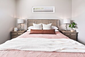 A neatly made bed with a white and pink bedspread, flanked by two bedside tables with lamps and a small clock on one.