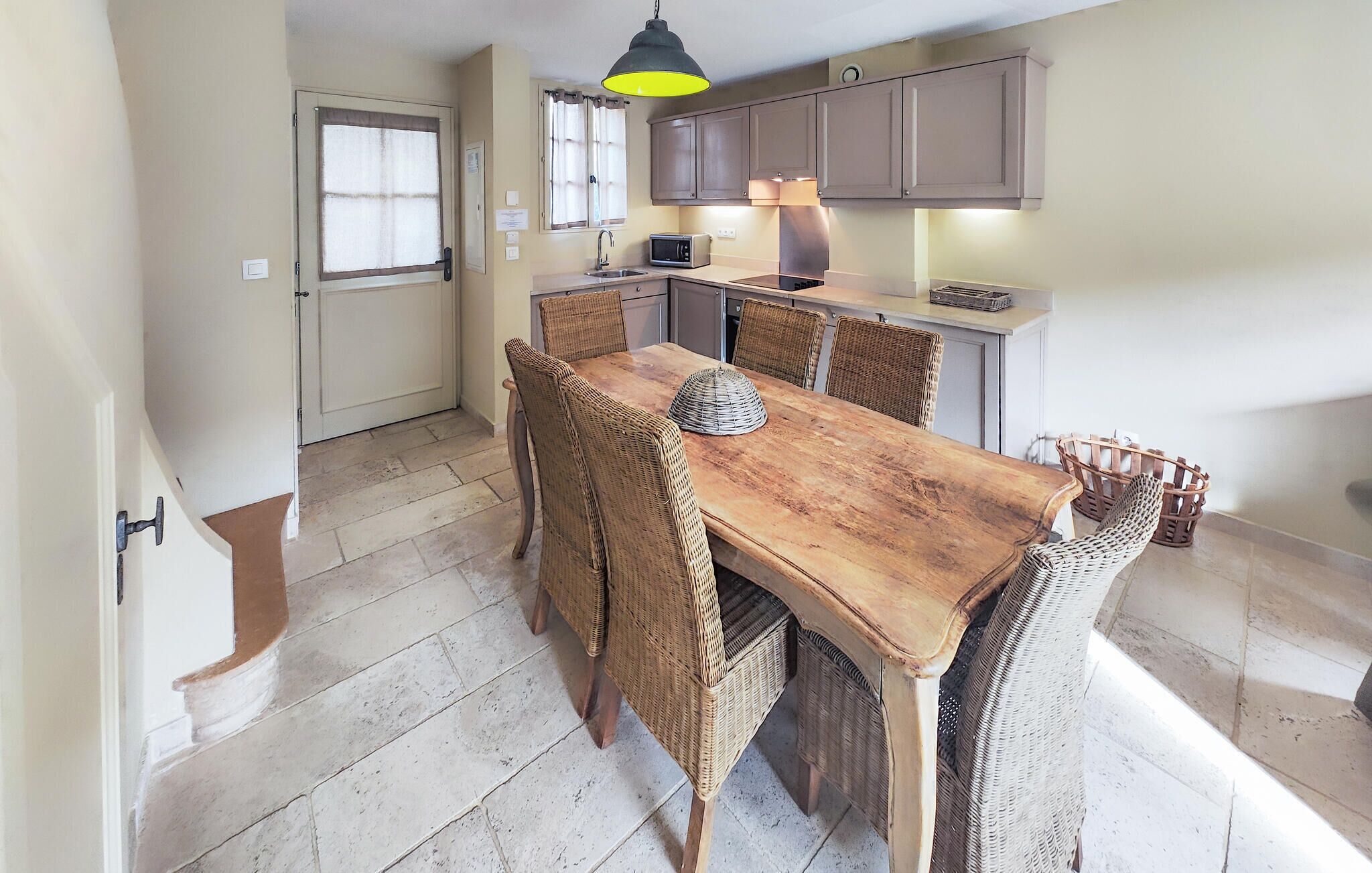 A dining area with a wooden table and wicker chairs, a kitchen with cabinets and appliances, and a door with a window.