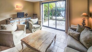 Ein Wohnzimmer mit Couchtisch aus Holz, zwei Sofas, einem Fernseher und einer großen Schiebeglastür zum Garten.