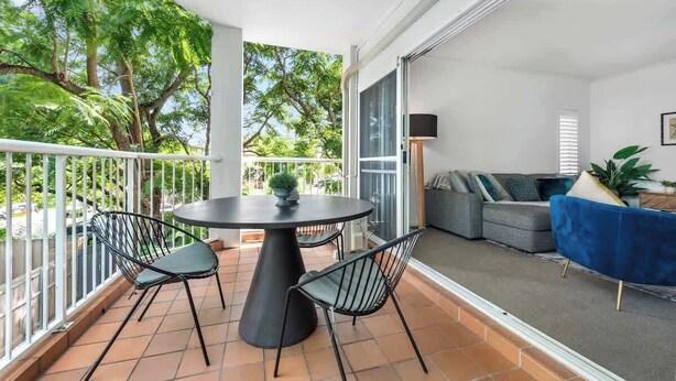 Un balcon avec une table ronde et des chaises, un canapé gris et une chaise bleue.