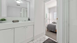 Une salle de bain avec un grand miroir, des meubles blancs, un lavabo et une petite plante.