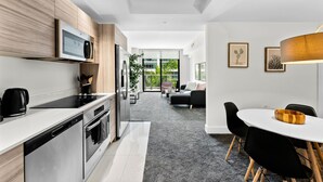 Una cocina moderna con microondas, horno y lavavajillas integrados. Hay una zona de comedor con una mesa blanca y sillas negras.