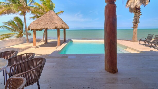 A poolside area with a thatched-roof structure, lounge chairs, and a view of the ocean. - Casa Kibis  -  Yucatan Home Rentals (Chicxulub)