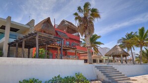 A beachfront property with a thatched-roof structure, a staircase leading to a building, and palm trees. - Casa Kibis  -  Yucatan Home Rentals (Chicxulub)