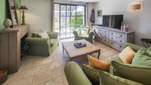 Una sala de estar con sofás verdes, una mesa de centro de madera, un televisor y un ventanal grande.