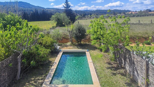 Piscina rectangular rodeada por una terraza de madera, con vista a un paisaje montañoso y un edificio distante.
