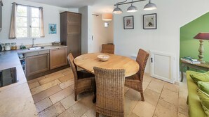Una cocina con una mesa redonda de madera, sillas de mimbre y un armario.