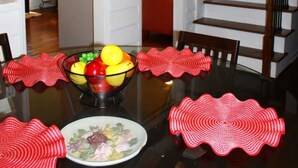A dining area with a glass table, red placemats, and a fruit bowl. A staircase is visible to the right. - Cozy, Relaxing 4-Bedroom House in Forest Park (Forest Park)