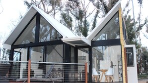 A modern house with large glass windows, a wooden deck, and a small outdoor seating area.