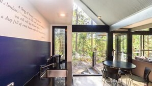 A modern kitchen with a black countertop and stainless steel appliances. There is a dining area with a round table and chairs, and a large window offering a view of the outdoors.
