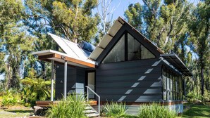 Une cabane moderne à deux étages, dotée d’un toit en pente, de grandes fenêtres et d’une terrasse en bois.