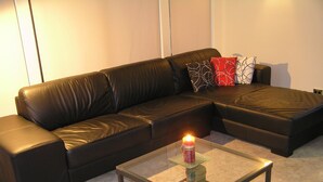 Un canapé d’angle en cuir noir, avec une table basse en verre placée devant.
