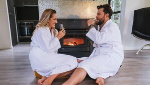 Un couple, vêtu de peignoirs blancs, est assis sur le sol devant une cheminée où le feu brûle.